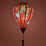 glowing balloon shaped lantern with red headed cranes in flight, pink and yellow flowers, firecrackers and orange lanterns