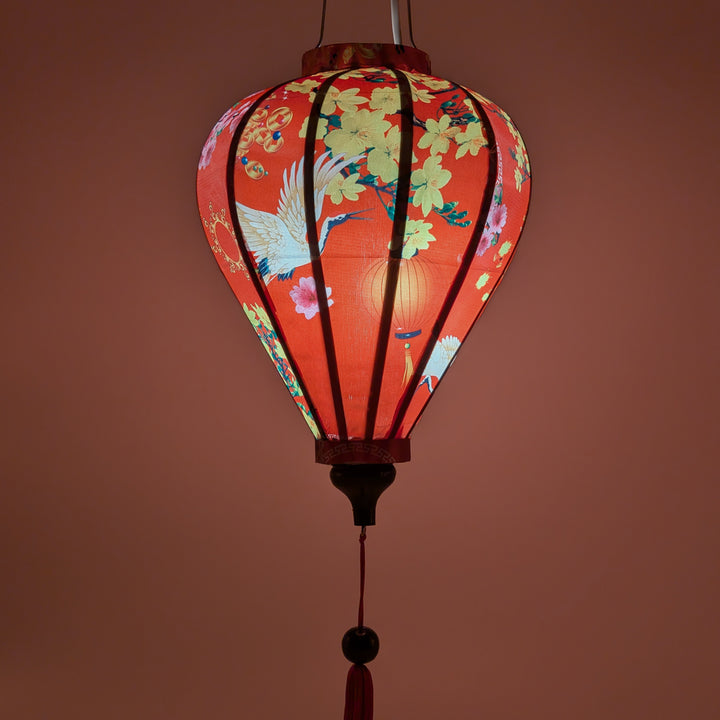 glowing balloon shaped lantern with red headed cranes in flight, pink and yellow flowers, firecrackers and orange lanterns