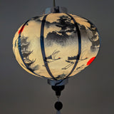 Up close of a round lantern featuring red-crowned cranes in flight, a pagoda, with crimson red sun lit from inside using an external light source creating a beautiful soft glow.