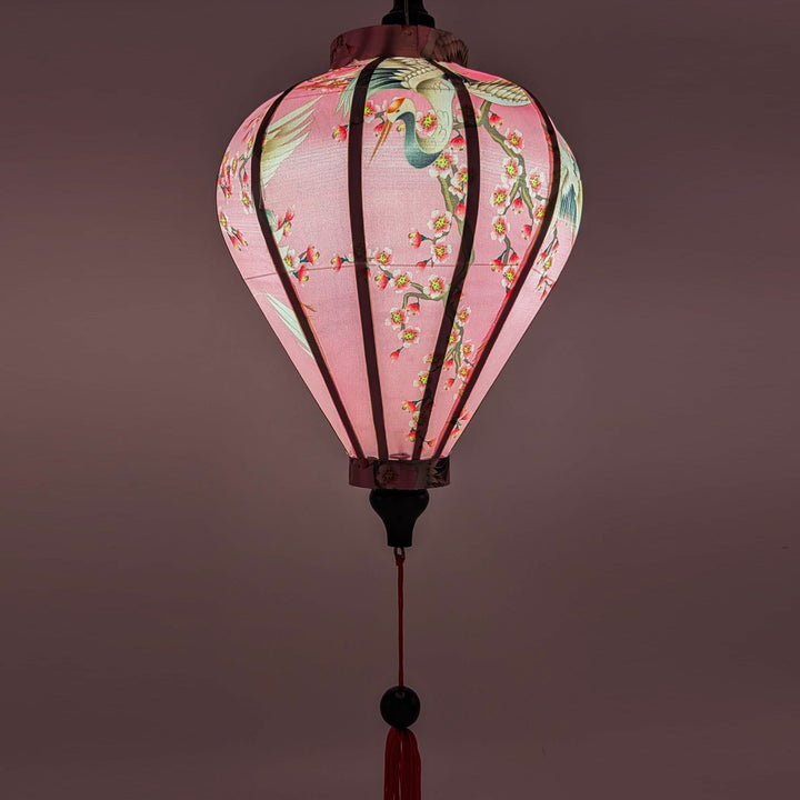 Upclose Balloon shaped lantern with a lightbulb placed inside creating a pink hue, lighting up the white cranes and flower blossoms on pink.