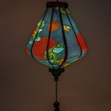 Close up of a glowing Teardrop shaped lantern with green and blue dragons on a black backdrop.