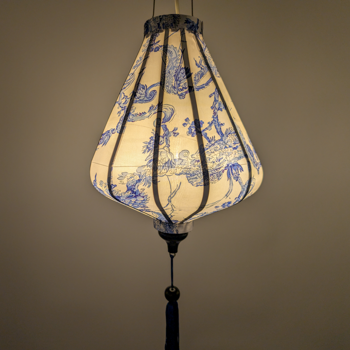 Glowing Teardrop shaped Vietnamese silk lantern with blue and white pattern on a plain white background.