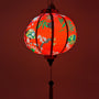 Up close red glowing Round Vietnamese lantern with red tassel with black, yellow and green lanterns and multi colour fans surrounded by white cherry blossoms on a bold red background.