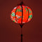 Up close red glowing Round Vietnamese lantern with red tassel with black, yellow and green lanterns and multi colour fans surrounded by white cherry blossoms on a bold red background.