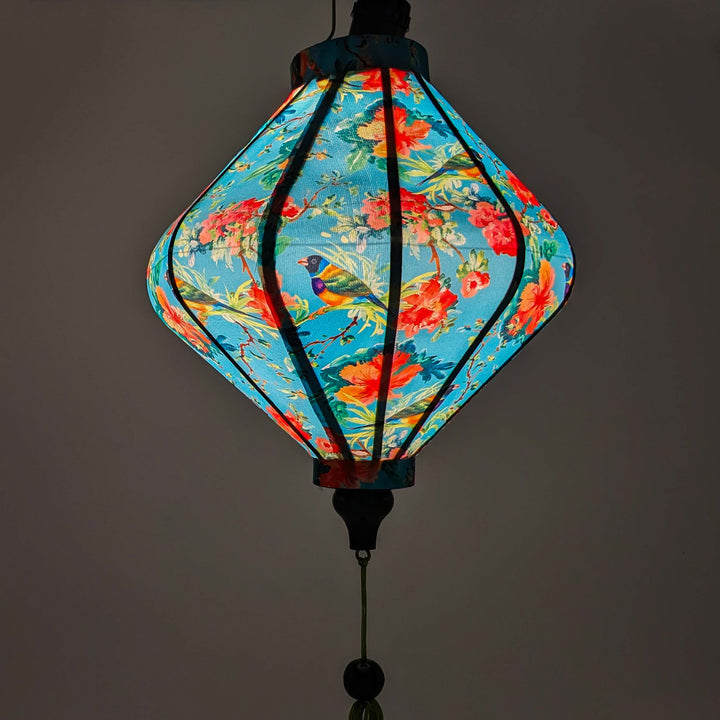 Glowing Lozenge shape lantern with finches in a hibiscus tree surrounded by pink and peach flowers in bloom.