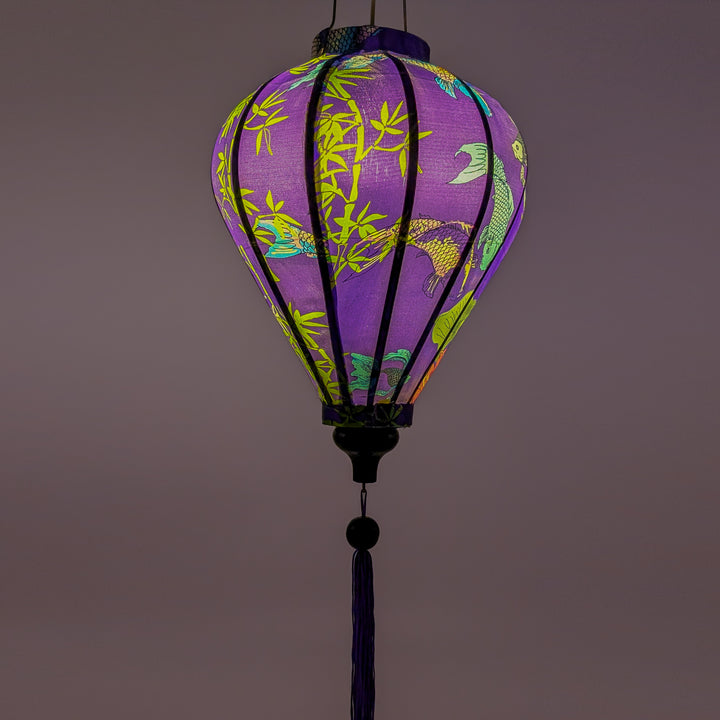 Glowing balloon shaped lantern with a print of koi fish swimming around bamboo reeds and pink lotus flowers on orange background.