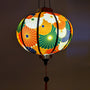 Glowing round Vietnamese lantern with flowers in colours orange, white, green, dark blue and gold outline.