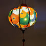 Glowing round Vietnamese lantern with flowers in colours orange, white, green, dark blue and gold outline.