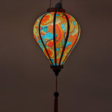 Up close glowing Balloon shaped Vietnamese lantern with red, blue, orange, green and yellow paisley print.