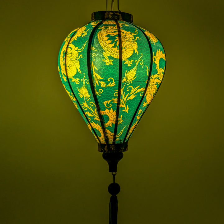 A close up of a glowing balloon shaped lantern with yellow dragons and green background.