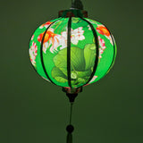 Up close of glowing handcrafted Hoi An lantern with goldfish and floral design on green background, perfect for garden decor.