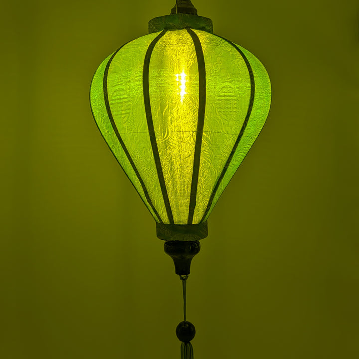 A green balloon shape Vietnamese lantern made from jacquard silk glowing.