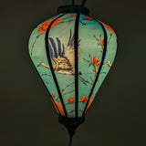 Glowing Vietnamese lantern featuring large herons flying amongst pink roses with a blue hue.