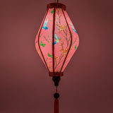 Glowing Tube shaped lantern with a print of hummingbirds mid-flight hunting nectar from orange flowers against striking pink background.