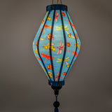 A glowing Tube shaped lantern with a print of dragonflies, lady bugs and bees on bright blue background.