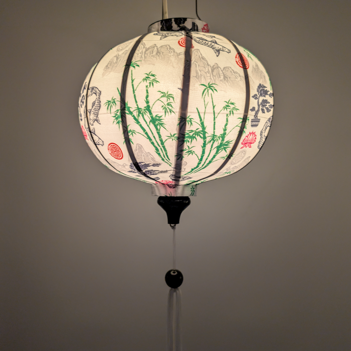 Glowing round Vietnamese silk lantern with koi fish and bamboo design on a white background