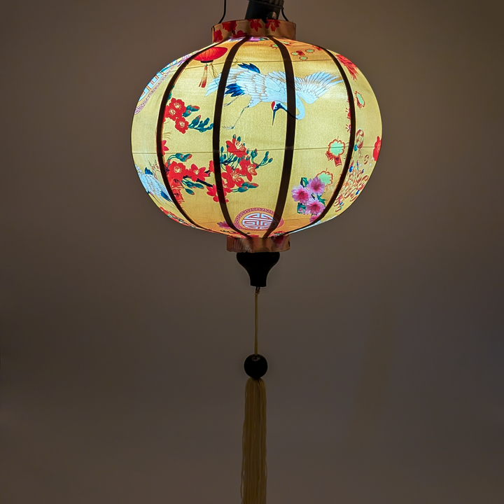 Glowing lantern with yellow hue adorned with elegant cranes, encircled by lanterns, and pink and red blossoms, all set against a backdrop of brilliant yellow. 
