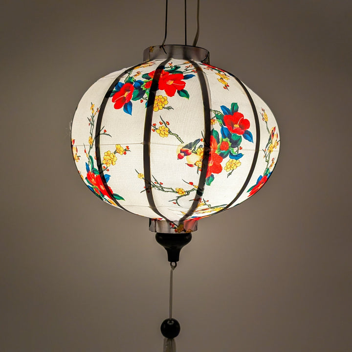A glowing round Vietnamese silk lantern adorned with a delicate floral pattern featuring vibrant red and yellow blossoms, handmade in Hoi An, Vietnam.