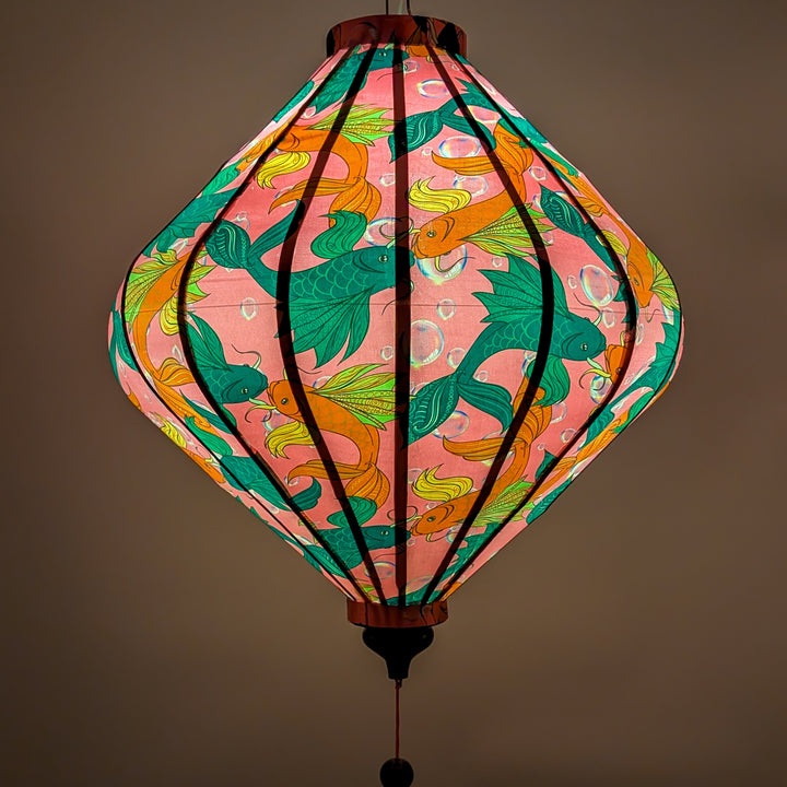 Glowing Lozenge shaped Vietnamese silk lantern with fish design on a pink background with iridescent bubbles.