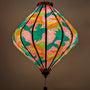Glowing Lozenge shaped Vietnamese silk lantern with fish design on a pink background with iridescent bubbles.