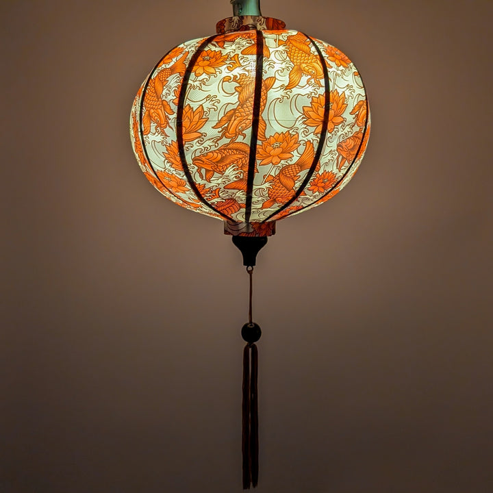Glowing Vietnamese silk lantern with orange koi fish and lotus flowers with gold background.