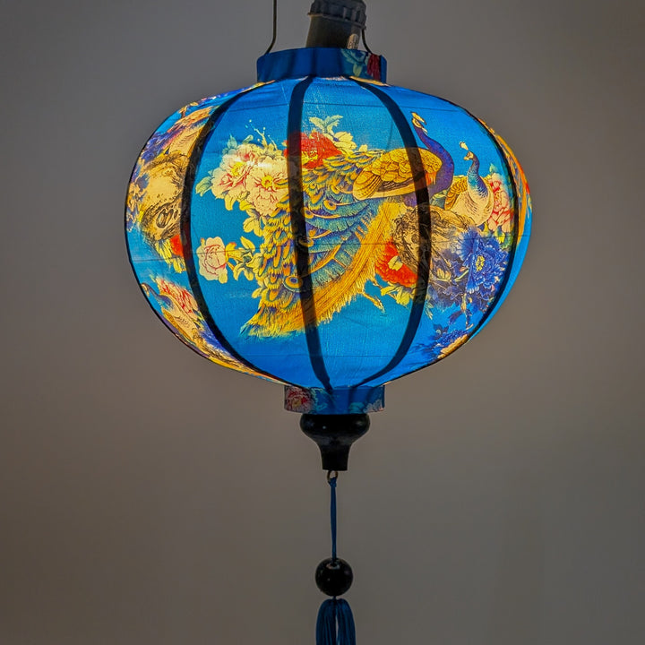 Glowing round Vietnamese silk lantern with vivid peacocks and blossoms in blue, pink and red on a deep blue background. 
