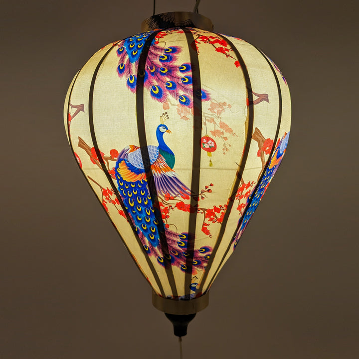 Glowing balloon shaped lantern with large flamboyant peacocks, dainty lanterns hanging on branches with pink and red on a cream background.