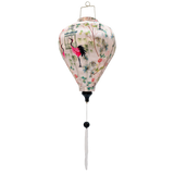 A balloon shaped Vietnamese lantern , handmade in Hoi An with vibrant fabric print featuring elegant pink and black cranes among lush green foliage and delicate blooming flowers. The scene is accented with traditional Asian-style pagodas, creating a serene yet bold aesthetic with rich colors.