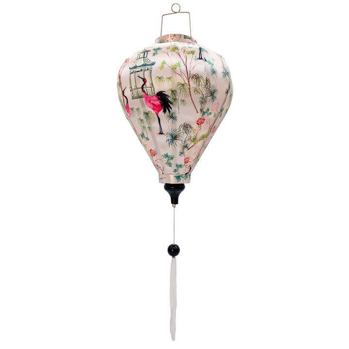 A balloon shaped Vietnamese lantern , handmade in Hoi An with vibrant fabric print featuring elegant pink and black cranes among lush green foliage and delicate blooming flowers. The scene is accented with traditional Asian-style pagodas, creating a serene yet bold aesthetic with rich colors.