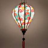 A glowing balloon shaped lantern with a print of pink flamingos and bird of paradise flowers on a light pink background.