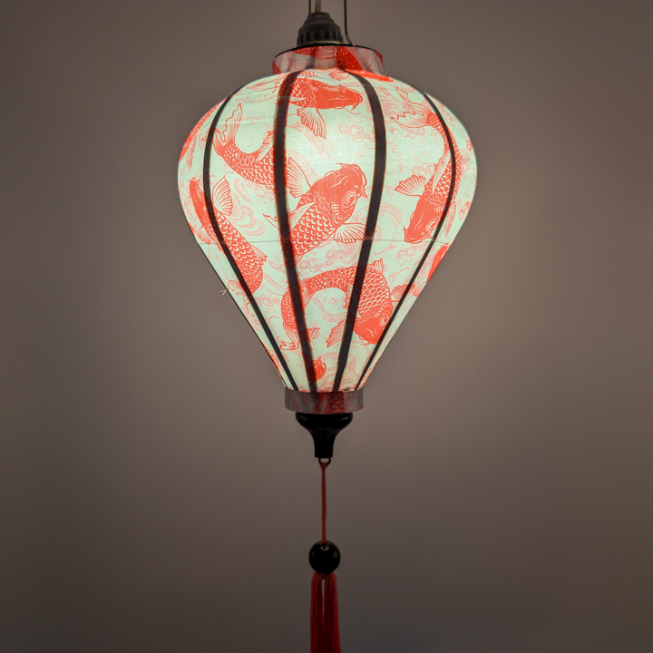 Glowing Vietnamese silk lantern with lightbulb placed inside featuring pink koi fish pattern on a white background