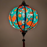 Glowing round Vietnamese lantern with print of red lotus flowers with against a deep, rich green background.