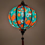 Glowing round Vietnamese lantern with print of red lotus flowers with against a deep, rich green background.