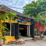 Traditional yellow building with open doors, tables, and chairs in a street setting with greenery and teal silk lanterns and red decorations in the tree.