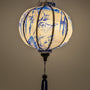 Glowing round Vietnamese silk lantern hand crafted in Hoi An, featuring a blue print of temples and pagodas high above hilltops with large bamboo trees floating against white background. 