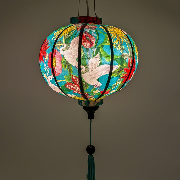 Glowing round Vietnamese silk lantern featuring vibrant cranes & floral print on blue.