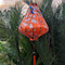 Teardrop shaped Vietnamese lantern hanging in front of palm leaves with print of bluebirds perched on a tree amidst white flower blossoms on orange.