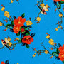 Polyester silk fabric with love birds sitting in a tree with red and yellow flowers on a bright blue background.