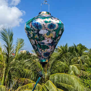 Diamond shaped lantern hanging high above palm trees with blue skies.