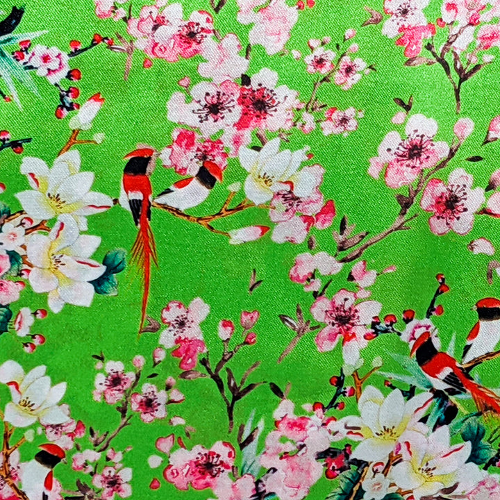 Polyester silk fabric with red-headed woodpecker birds sitting in cherry blossom trees on a bright green background.