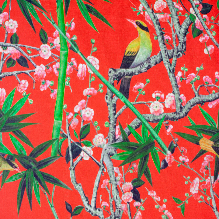 Polyester silk fabric with Blacknaped Oriole birds perched in a tree filled with pink flowers and surrounded by green bamboo plants on striking red.