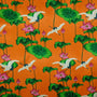 Orange polyester silk fabric with white cranes surrounded by pink flowers with large green leaves.