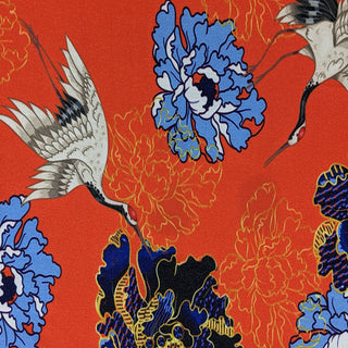 Polyester silk fabric with white red-headed cranes, surrounded by gold and blue flowers on a red background. 